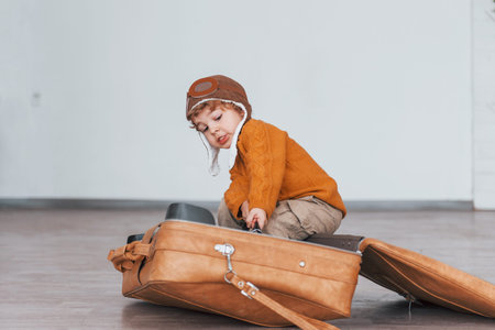 Little boys in retro pilot costume have fun and sitting in suitcase indoors at daytimeの写真素材