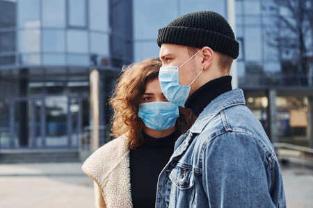 Couple in protective masks have a walk outdoors in the city near business building at quarantine time. Conception of coronavirusの写真素材