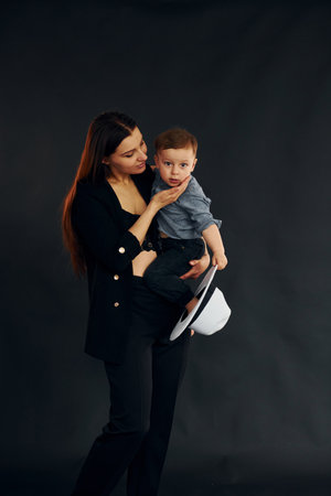 Mother in stylish black clothes is with her little son in the studioの写真素材