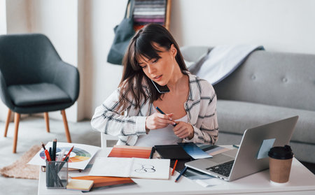 Sits by table. Young female freelance worker is indoors in home at daytimeの写真素材
