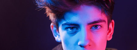 Portrait of young beautiful guy with fashionable haircut. Neon lightingの写真素材