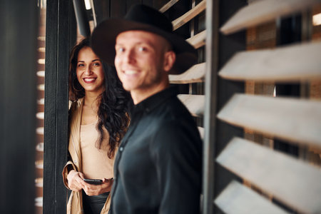 Woman with black curly hair and her man standing together near wooden windowsの写真素材