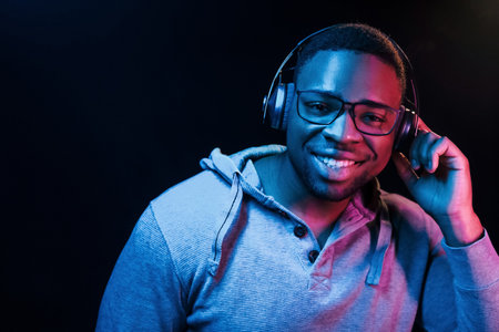 With headphones. Futuristic neon lighting. Young african american man in the studioの写真素材