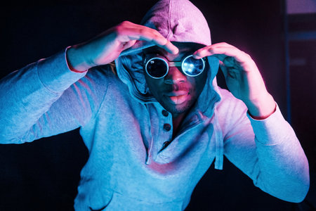 Cyberpunk style glasses. Futuristic neon lighting. Young african american man in the studioの写真素材