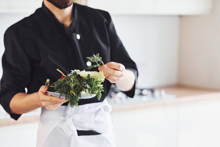 With vegetables. Professional young chef cook in uniform working on the kitchenの写真素材