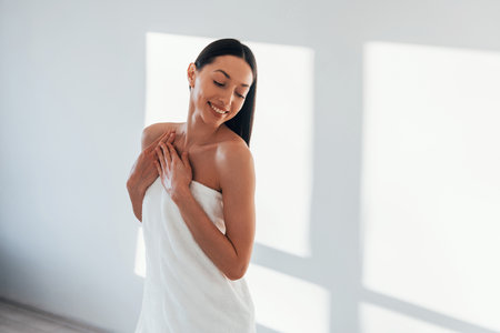 In room with white walls. Young caucasian woman with slim body shape is indoors at daytimeの写真素材