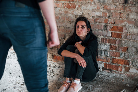 Violent man standing and threatens girl that sits on the floor with teddy bear in abandoned buildingの写真素材