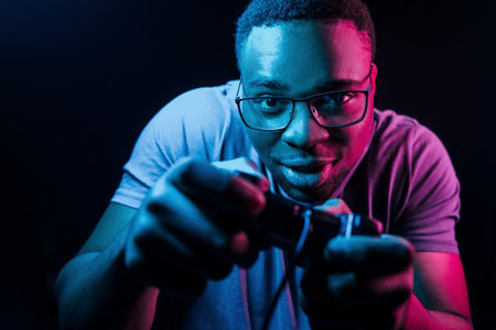 Plays game by using controller. Futuristic neon lighting. Young african american man in the studioの写真素材