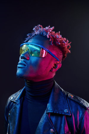 In glasses. Futuristic neon lighting. Young african american man in the studio