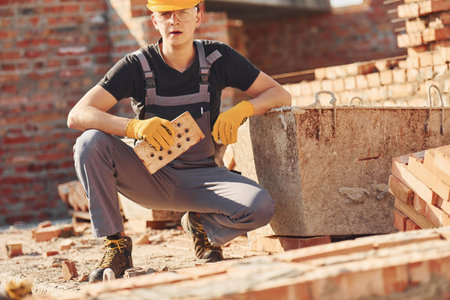Construction worker in uniform and safety equipment sits and have job on buildingの写真素材
