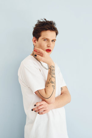 Young gay man is standing in the studio and posing for a camera. Lips in red lipstickの写真素材