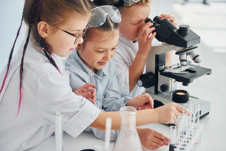 Side view. Children in white coats plays a scientists in lab by using equipmentの写真素材