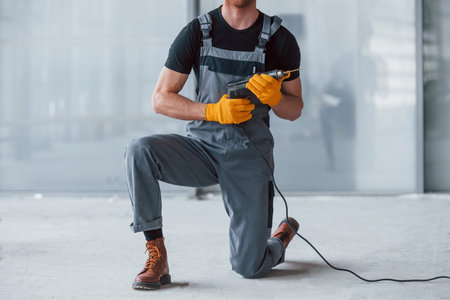 Close up view of man in grey uniform with drill in hand indoors in modern big office at daytimeの写真素材
