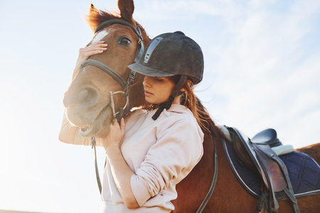 Beautiful sunshine. Young woman standing with her horse in agriculture field at daytimeの写真素材