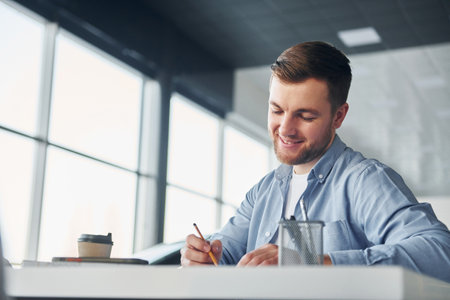 Young man in white shirt and blue jacket works indoorsの写真素材