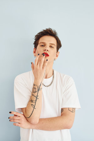 Young gay man is standing in the studio and posing for a camera. Lips in red lipstickの写真素材