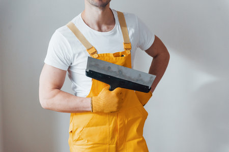 Handyman in yellow uniform standing against white wall. House renovation conceptionの写真素材