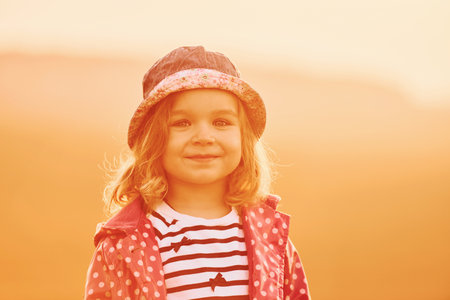 Portrait of cute little girl that standing outdoors illuminated by orange sunlightの写真素材