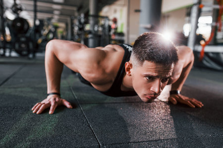 Doing push-ups. Young sportive strong man in black wear have workout day in gym