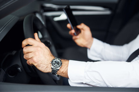 Successful man. Young guy in white shirt is sitting inside of a modern new automobileの写真素材