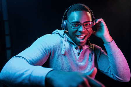 With headphones. Futuristic neon lighting. Young african american man in the studioの写真素材
