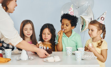 Woman holds cake. Children on celebrating birthday party indoors have fun togetherの写真素材