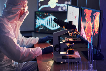 Monitors with information on the table. Scientist in white protective uniform works with coronavirus...