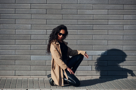 Beautiful brunette with curly hair and in black clothes outdoors near wallの写真素材