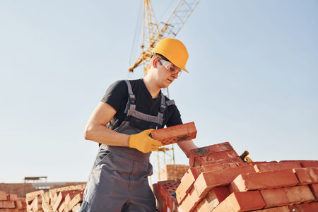 Installing brick wall. Construction worker in uniform and safety equipment have job on building