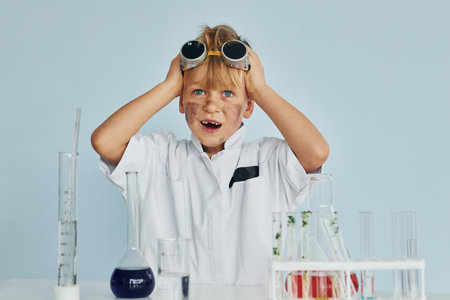 Scared little boy in coat playing a scientist in lab by using equipmentの写真素材