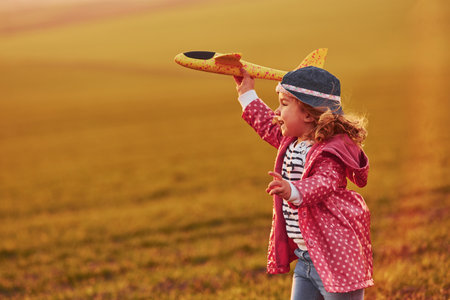 Cute little girl have fun with toy plane on the beautiful field at sunny daytimeの写真素材