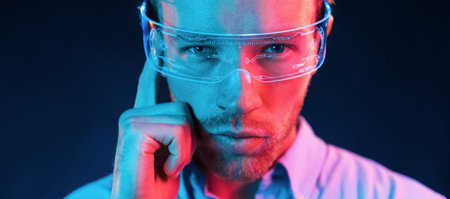 In glasses with display. Neon lighting. Young european man is in the dark studioの写真素材