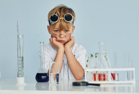 Scared little boy in coat playing a scientist in lab by using equipmentの写真素材