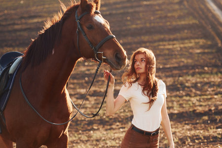 Young woman standing with her horse in agriculture field at sunny daytimeの写真素材