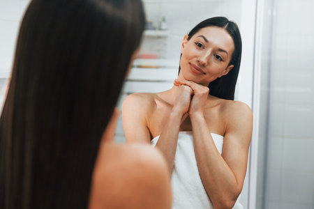 Making care of her skin. Young caucasian woman with slim body shape is indoors at daytimeの写真素材