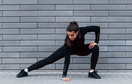 Young sportive girl in black sportswear outdoors doing stretching near gray wallの写真素材