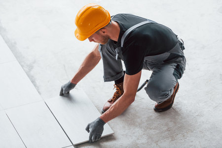 Installation of plates. Man in grey uniform and orange hard hat works indoors in modern big office at daytimeの写真素材