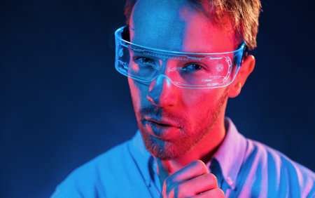 In glasses with display. Neon lighting. Young european man is in the dark studio