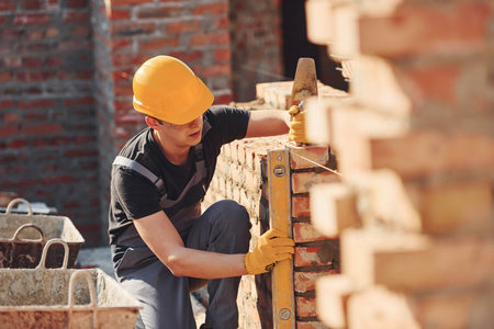 Measures of brick wall. Construction worker in uniform and safety equipment have job on buildingの写真素材