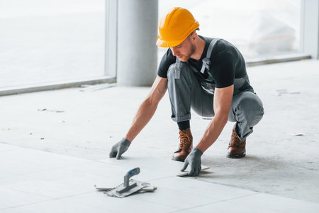 Installation of plates. Man in grey uniform and orange hard hat works indoors in modern big office at daytimeの写真素材