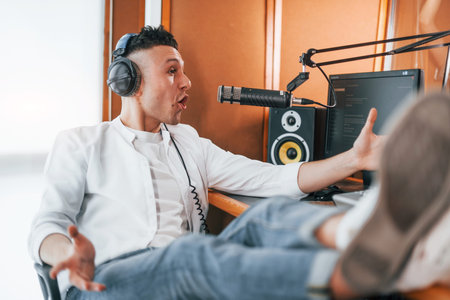 Talks and uses mic. Young man is indoors in the radio studio is busy by broadcast