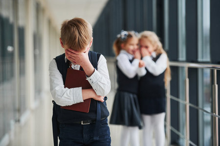 Little boy gets bullied. Conception of harassment. School kids in uniform together in corridorの写真素材