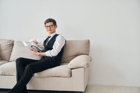 Young man in formal clothes sits on the sofa indoors against white wallの写真素材