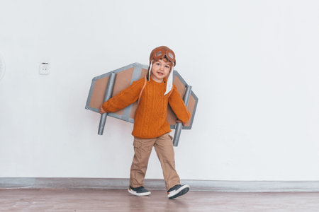 Little boy in retro pilot uniform running with toy plane indoors