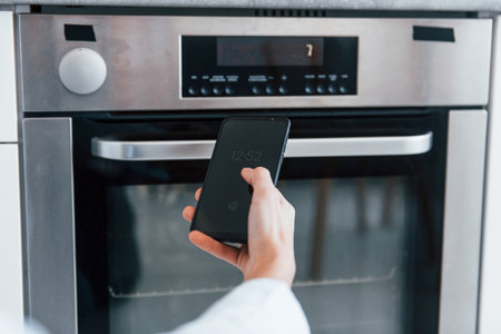 Young woman is indoors in smart house room controlling the ovenの写真素材