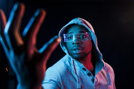 In special eyewear. Futuristic neon lighting. Young african american man in the studioの写真素材