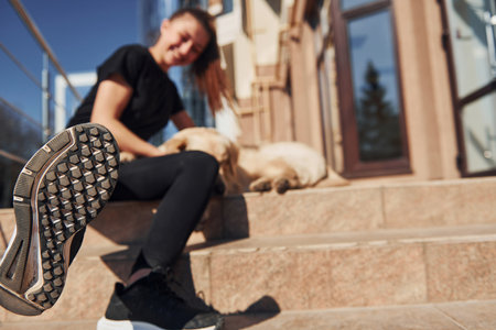 Sitting together. Young positive woman have fun with her dog when have a walk outdoors near business buildingの写真素材