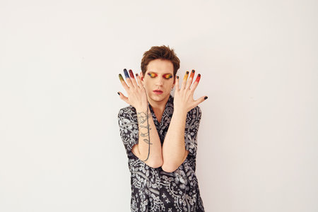 Young gay man is standing in the studio and posing for a camera. Multicolored make up on face fingersの写真素材