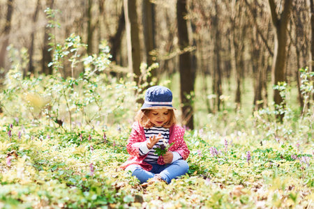 Happy little girl in blue hat have walk in spring forest at daytimeの写真素材