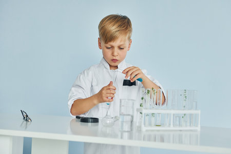 Uses test tubes. Little boy in coat playing a scientist in lab by using equipmentの写真素材